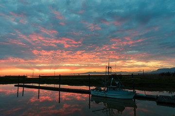 fishing boat on the pier at the pier with a reflection in the water against the evening sky, at dusk with a glow and clouds,