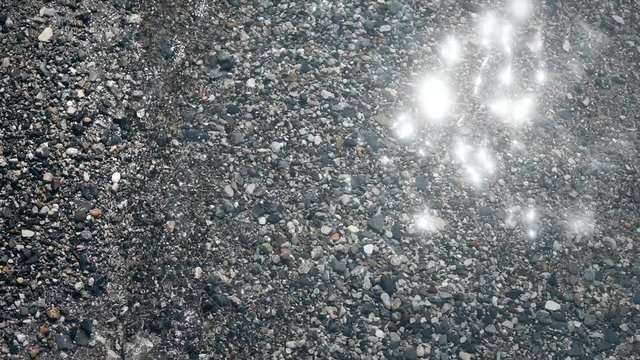 4K footage of some rocks under water, in a lake shore, with small waves and sunlight.