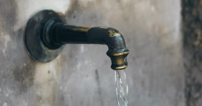 4K footage of some water running from an old faucet of a public fountain.