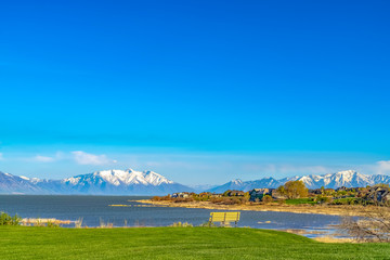 Empty bench and houses on the lush field surrounding a vast lake