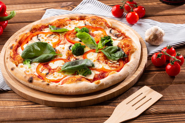 Vegetarian pizza on a wooden background with mushrooms, broccoli, cheese and sweet pepper and basil. Top view.