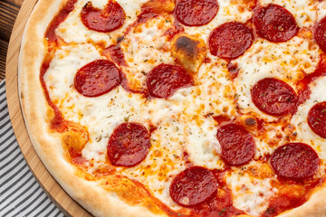 Delicious hot homemade Pepperoni pizza on the wooden table. Pepperoni Pizza - Fresh homemade pizza with pepperoni, cheese and tomato sauce on rustic black stone background wirh copy space.  