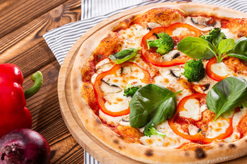 Vegetarian pizza on a wooden background with mushrooms, broccoli, cheese and sweet pepper and basil. Top view.