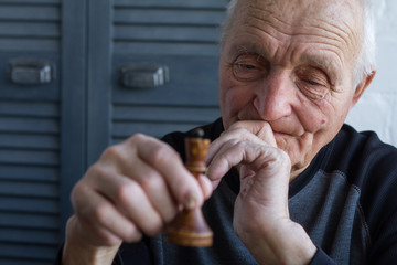 The old man holds in his hands the chess piece of the king, the concept of winning or losing
