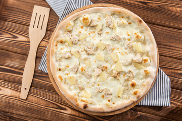 Pizza topped with sauce, chicken, cheese and pineapple serve on wooden plate on wooden table. Photo of Hawaiian pizza. 