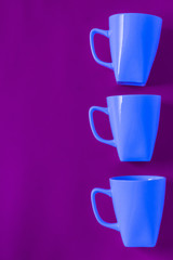 3 blue winter coffee cup mugs lined up in a row for a break time meeting; Copyspace with empty room space for copy text on purple vertical background