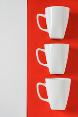 3 white winter coffee cup mugs lined up in a row for a break time meeting; Copyspace with empty room space for copy text on red vertical background; Christmas holiday or Valentines.