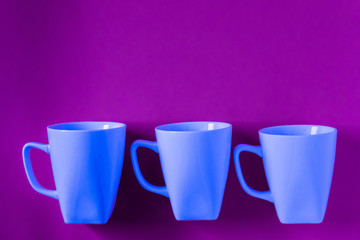 3 blue winter coffee cup mugs lined up in a row for a break time meeting; Copyspace with empty room space for copy text on purple horizontal background