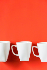 3 white winter coffee cup mugs lined up in a row for a break time meeting; Copyspace with empty room space for copy text on red vertical background; Christmas holiday or Valentines.