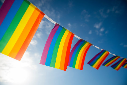 Gay pride rainbow flag bunting fluttering in the sky backlit by golden sun