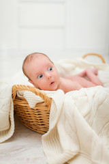 Newborn naked baby is lying in wicker basket. Basket on white wooden background. Newborn photo shoot