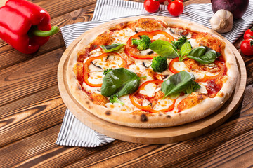 Vegetarian pizza on a wooden background with mushrooms, broccoli, cheese and sweet pepper and basil. Top view.