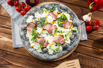 Top view of delicious Pizza on wooden table. Tasty pizza with ham, corn, rucola and cheese. Black pizza.