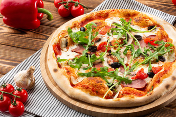 Pizza with ham , arugula (salad rocket), rucola, mushrooms olives and mozzarella  on  wooden background close up. Italian cuisine.