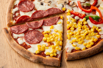 Delicious italian pizza with meat, vegetables  cheese 4 seasons isolated on wooden background. Quattro Stagioni pizza with mozzarella, ham, bacon, mushrooms, salami, mozzarella, corn, sweet pepper . 