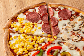 Delicious italian pizza with meat, vegetables  cheese 4 seasons isolated on wooden background. Quattro Stagioni pizza with mozzarella, ham, bacon, mushrooms, salami, mozzarella, corn, sweet pepper . 