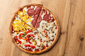 Delicious italian pizza with meat, vegetables  cheese 4 seasons isolated on wooden background. Quattro Stagioni pizza with mozzarella, ham, bacon, mushrooms, salami, mozzarella, corn, sweet pepper . 