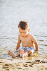 Theme is summer time and rest near the water. Little joyful Caucasian funny boy plays and enjoys in the river. The child is resting and swimming in the lake pond sandy beach