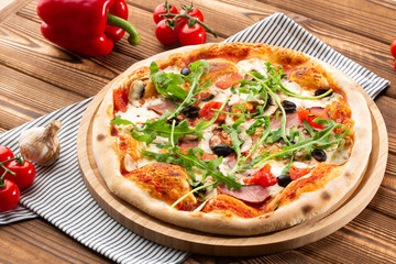 Pizza with ham , arugula (salad rocket), rucola, mushrooms olives and mozzarella  on  wooden background close up. Italian cuisine.