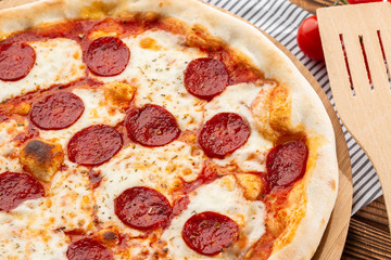 Delicious hot homemade Pepperoni pizza on the wooden table. Pepperoni Pizza - Fresh homemade pizza with pepperoni, cheese and tomato sauce on rustic black stone background wirh copy space.  