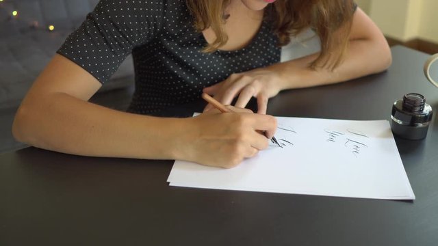 Close up shot of a young woman calligraphy writing on a paper using lettering technique. She writtes I love you