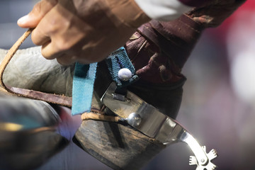 A close up of a cowboy boot and spur on a pipe.