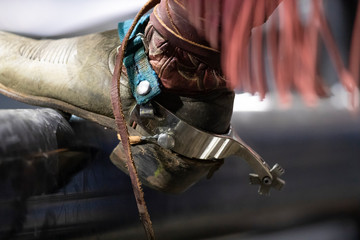 A close up of a cowboy boot and spur on a pipe.