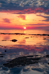 Beautiful red sunset. The sun is setting in the sea. Reflection in the sea, rocky shore. Sun rays.