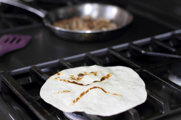 Flour tortilla cooking directly over the flame on a natural gas stove oven.