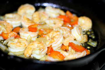 Shrimp cooking with red bell peppers and onion in a cast iron skillet on the stove.