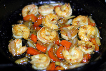 Shrimp cooking with red bell peppers and onion in a cast iron skillet on the stove.