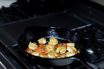 Shrimp cooking with red bell peppers and onion in a cast iron skillet on the stove.