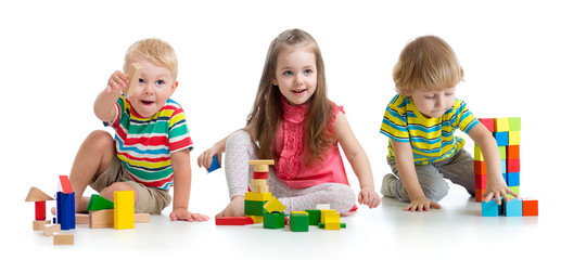 Cute little children playing with toys or blocks and having fun while sitting on floor isolated over white background