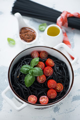 Squid-ink spaghetti with cherry tomatoes and basil over white concrete background, vertical shot