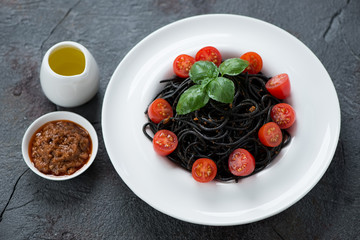 Plate of squid-ink spaghetti with sun dried tomatoes pesto, studio shot over grey stone background