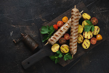 Grilled chicken kabobs with roasted mini potato and cherry tomatoes, flatlay over dark brown stone background with space