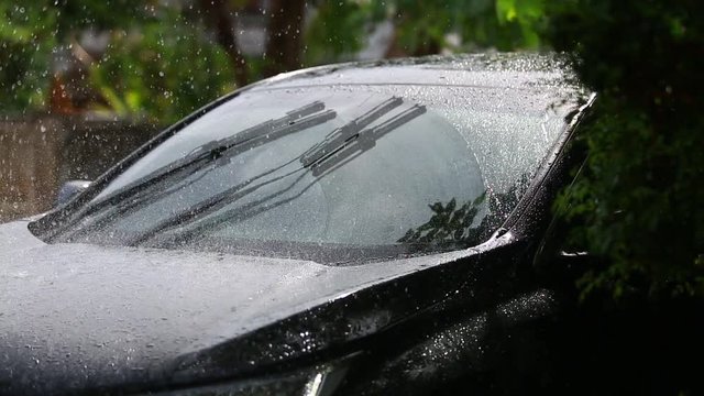 Car windshield with rain drops and frameless wiper blade closeup.