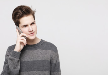 Smiling man in t-shirt talking by smartphone over grey background