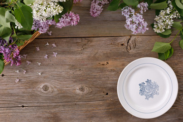 Fototapeta na wymiar Plate and decor of flowers on the background of vintage wooden planks.Vintage background with lilac flowers and place under the text. View from above. Flat lay. Cutlery.