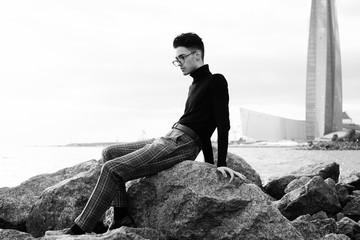   fashionable young man sitting on the rocks near the sea