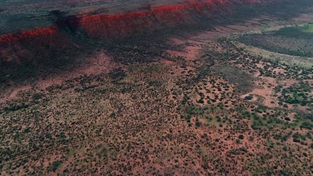 Aerial Forward/Pan Up: Red Mountains On Large Plain With Cloudy Sky Above - Uluru, Australia