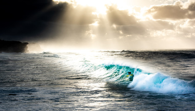 Surfer catching wave at Bronte Beach Sydney Australia with rays of sunrise highlighting surfer