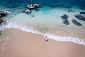 Obraz premium Young woman in a dress lying on the back on the white sand near the waves of blue sea. Top view, Andaman Sea, Phuket, Thailand. Aerial
