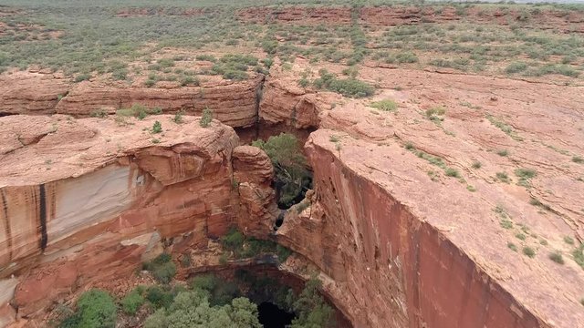 Aerial Forward/Pan Up: Large Hole Surrounded By Cliffs Leading Up To Plain - Uluru, Australia