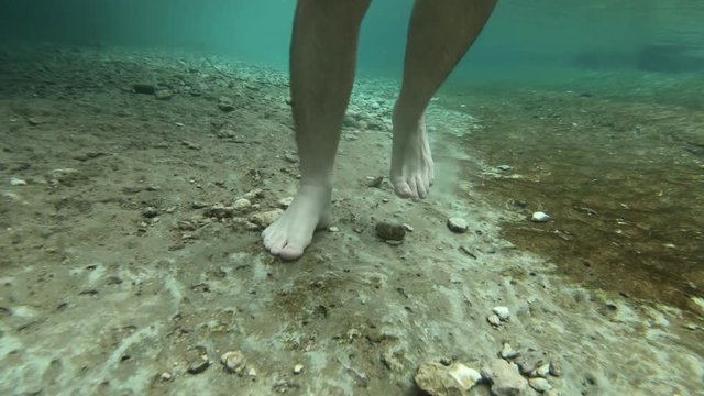 Man feet walking on slippery riverbed, underwater shot 