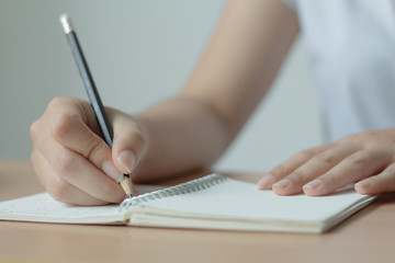 Female hand with pen writing on notebook.Woman Wearing white T-shirt.