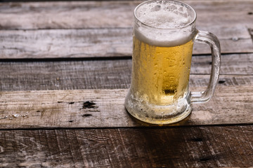 Chilled beer in mug with ice cold drops over a wood surface