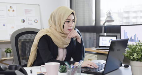 Serious concerned young islam businesswoman look on laptop screen in deep thought sitting at...
