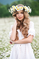 Beautiful young girl with curly hair in chamomile field.  Beautiful girl with chamomile wreath on...