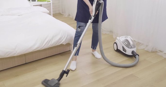 tired asian woman cleaning wooden floor with vacuum cleaner in bedroom. sick housemaid frowning face with low back pain while doing house chores working in day time. illness lady with backache hurt